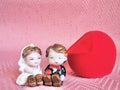 Bride and groom porcelain dolls with ring box on pink background.