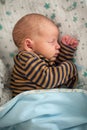 Cute little calm baby in a striped baby clothes, peacefully sleeping soundly in his crib with his toys in a bright room