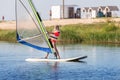 Cute little caucasian blond child girl enjoy having fun learning to surf on winsurfing board at freshwater pond lake or