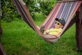 Cute little Caucasian boy relaxing and having fun in multicolored hammock in backyard or outdoor playground. Summer active leisure