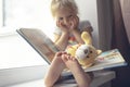 Cute little caucasian child sits near window and reads book. Royalty Free Stock Photo