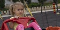 Cute caucasian child swings on swing, with sad and upset expression.