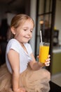 Cute little caucasian girl with blonde hair sitting on the kitchen table and drinking fresh mango juice. Healthy lifestyle concept Royalty Free Stock Photo