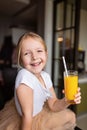 Cute little caucasian girl with blonde hair sitting on the kitchen table and drinking fresh mango juice. Healthy lifestyle concept Royalty Free Stock Photo