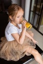 Cute little caucasian girl with blonde hair sitting on the kitchen table and drinking fresh mango juice. Healthy lifestyle concept Royalty Free Stock Photo