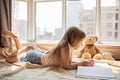 Cute little caucasian girl in casual clothes reading a book with stuffed teddy bear toy and smiling while lying on a floor near Royalty Free Stock Photo