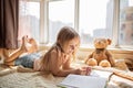 Cute little caucasian girl in casual clothes reading a book with stuffed teddy bear toy and smiling while lying on a floor near Royalty Free Stock Photo