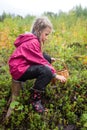 Cute little caucasian girl is picking wild berries sitting on a tree stump Royalty Free Stock Photo