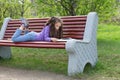 Cute little caucasian girl reading book lying on a bench in spring park Royalty Free Stock Photo