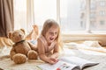 Cute little caucasian girl reading a book with stuffed teddy bear toy. Stay at home during coronavirus covid-19 pandemic Royalty Free Stock Photo