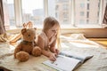 Cute little caucasian girl reading a book with stuffed teddy bear toy. Stay at home during coronavirus covid-19 pandemic Royalty Free Stock Photo