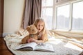 Cute little caucasian girl reading a book with stuffed teddy bear toy. Stay at home during coronavirus covid-19 pandemic Royalty Free Stock Photo