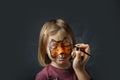 Cute little caucasian girl with tiger face painting on the black background. Close up portrait of little kid with face-painting.