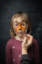 Cute little caucasian girl with tiger face painting on the black background. Close up portrait of little kid with face-painting.