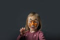 Cute little caucasian girl with tiger face painting on the black background. Close up portrait of little kid with face-painting.