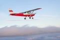 Cute little Cessna airplane flying away over a coudy hilly terrain Royalty Free Stock Photo