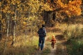 Cute little child boy and his father runs on a rural road in autumn forest. Time together dad and son outdoor in fall season. View Royalty Free Stock Photo