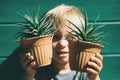 Cute little child boy holding two pots with succulent haworthia plants on green wall background. Indoor home gardening, kid with