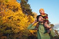 Cute little child boy sitting on his father`s shoulders on background of beautiful autumn forest. Time together dad and son Royalty Free Stock Photo