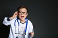 Cute little child in doctor uniform with reflex hammer on black background.