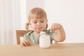 Cute little child eating tasty yogurt with spoon at wooden table indoors