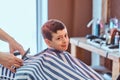 Cute little child is getting trendy haircut from barber at busy barbershop