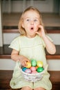 Cute little child girl with blonde hair on Easter day. Girl holding basket with painted eggs and sitting on the stairs at home Royalty Free Stock Photo