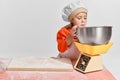 Cute little child, girl in image of chef cooking over grey background. Measuring flour