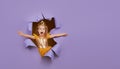 Cute little child girl in princess costume breaks through a colored purple paper wall. Points with a magic wand to the empty space Royalty Free Stock Photo