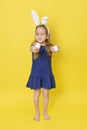 Cute little child girl wearing bunny ears on Easter day. Girl holding painted eggs with emoji for easter on yellow background.