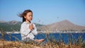 Cute little child gurl meditating alone in lotus pose at lake shore