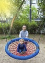 Cute little child with his mother having fun on a colorful swing outdoor in the park. Beautiful spring day in children playground Royalty Free Stock Photo