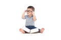 Cute little child play with book and wearing glasses while sitting on floor isolated over white background, Royalty Free Stock Photo