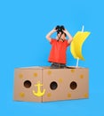 Cute little child playing with binoculars and cardboard ship on blue background Royalty Free Stock Photo