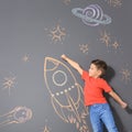 Cute little child playing with chalk rocket drawing on grey Royalty Free Stock Photo