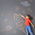 Cute little child playing with chalk rocket drawing on grey Royalty Free Stock Photo