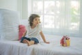 Cute little child sitting on bed with gift box at home, take congratulations on your birthday