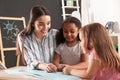 Cute little children with nursery teacher reading book at table in kindergarten Royalty Free Stock Photo
