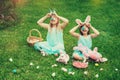 Cute little children wearing bunny ears on Easter day sitting on grass in garden. Girls holding painted eggs cover their Royalty Free Stock Photo