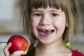 A cute little curly toothless girl smiles and holds a red apple. Portrait of a happy baby eating a red apple. The child loses milk Royalty Free Stock Photo