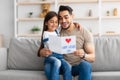 Cute little daughter greeting young dad with card