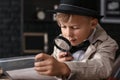 Cute little detective working with evidence at table