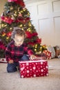 Cute little diverse boy opening a magical Christmas present in front of a Christmas tree Royalty Free Stock Photo