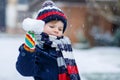 Cute little funny kid boy in colorful winter fashion clothes having fun and playing with snow, outdoors during snowfall Royalty Free Stock Photo