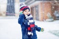 Cute little funny kid boy in colorful winter fashion clothes having fun and playing with snow, outdoors during snowfall Royalty Free Stock Photo