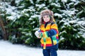 Cute little funny kid boy in colorful winter fashion clothes having fun and playing with snow, outdoors during snowfall Royalty Free Stock Photo