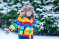 Cute little funny kid boy in colorful winter fashion clothes having fun and playing with snow, outdoors during snowfall Royalty Free Stock Photo