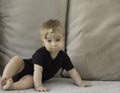 Cute little funny serious caucasian blonde baby girl, blue eyes, sitting on background of beige soft sofa pillows in Royalty Free Stock Photo