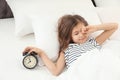 Cute little girl with alarm clock awaking in bed Royalty Free Stock Photo