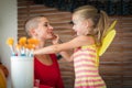 Cute little girl applying face paint to her mothers face for Halloween party. Halloween or carnival family lifestyle background.